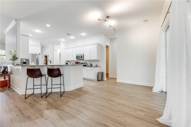 kitchen featuring white cabinetry, stainless steel appliances, light stone counters, kitchen peninsula, and light wood-type flooring