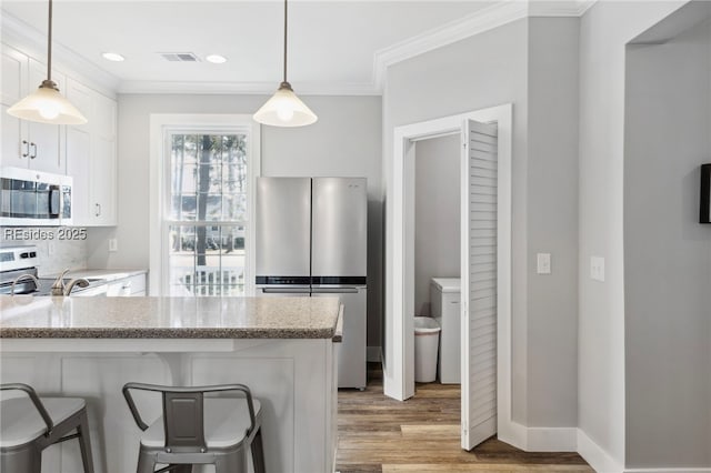 kitchen with appliances with stainless steel finishes, decorative light fixtures, white cabinets, a kitchen bar, and light stone counters