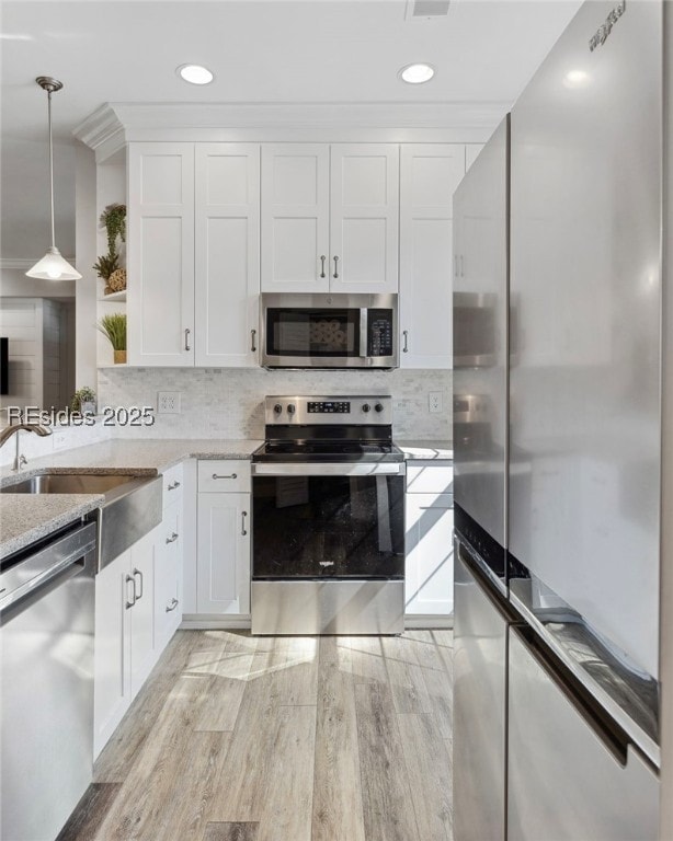 kitchen featuring sink, appliances with stainless steel finishes, white cabinetry, hanging light fixtures, and light hardwood / wood-style floors