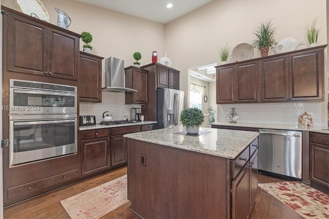 kitchen with a kitchen island, hardwood / wood-style floors, stainless steel appliances, dark brown cabinets, and wall chimney exhaust hood