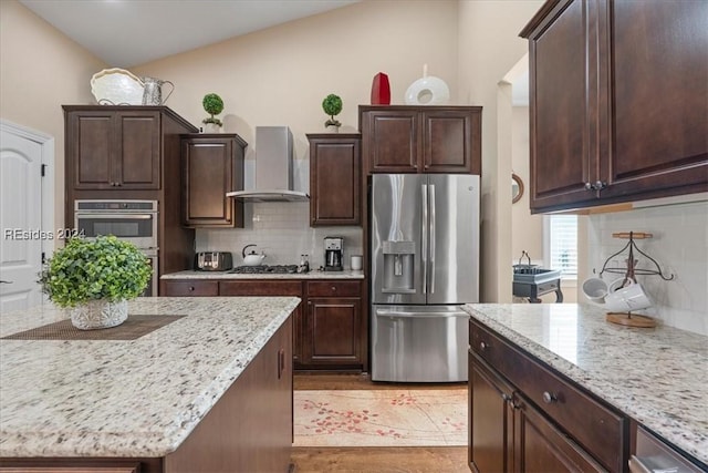 kitchen featuring appliances with stainless steel finishes, tasteful backsplash, lofted ceiling, light stone counters, and wall chimney exhaust hood