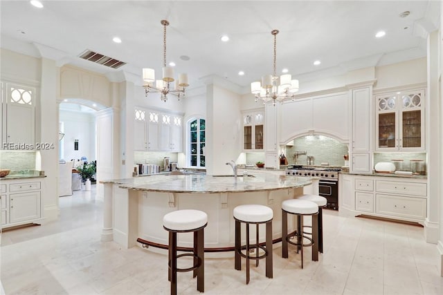 kitchen with tasteful backsplash, decorative light fixtures, range with two ovens, and a large island with sink