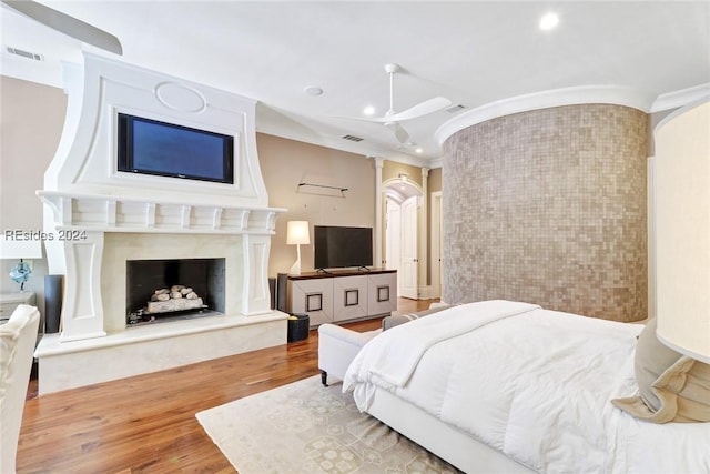 bedroom featuring crown molding, hardwood / wood-style flooring, ceiling fan, brick wall, and a fireplace