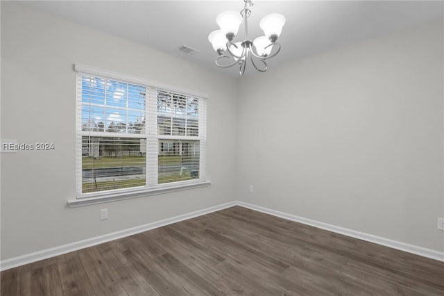 spare room featuring an inviting chandelier and dark hardwood / wood-style floors