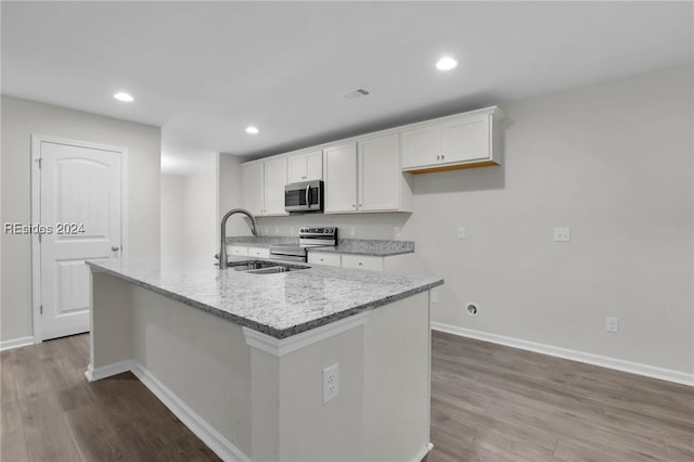 kitchen featuring appliances with stainless steel finishes, white cabinets, a kitchen island with sink, light stone counters, and light hardwood / wood-style flooring