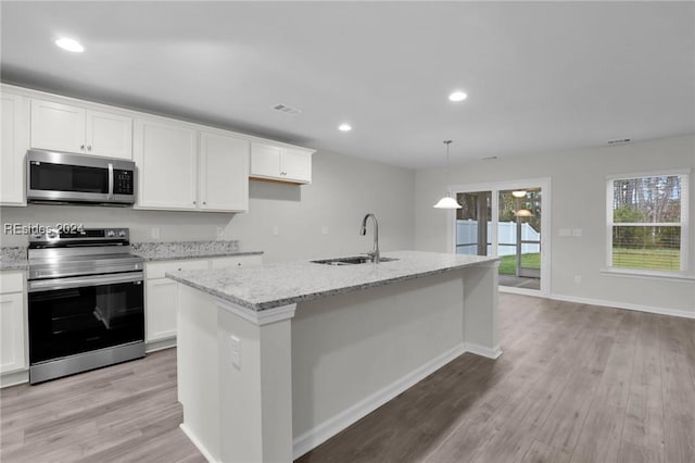 kitchen featuring sink, appliances with stainless steel finishes, white cabinetry, a center island with sink, and decorative light fixtures