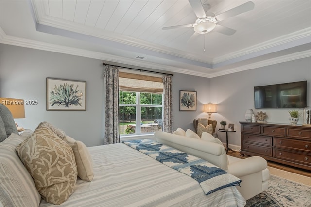 bedroom featuring hardwood / wood-style flooring, ornamental molding, ceiling fan, and a tray ceiling