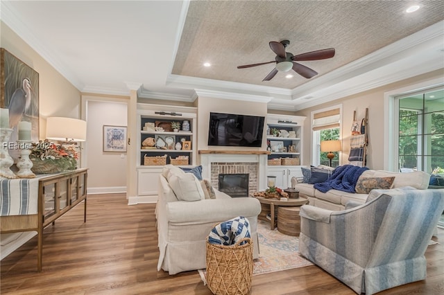 living room with a raised ceiling, ornamental molding, hardwood / wood-style flooring, and a fireplace