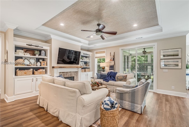 living room featuring hardwood / wood-style flooring, crown molding, built in features, and a tray ceiling