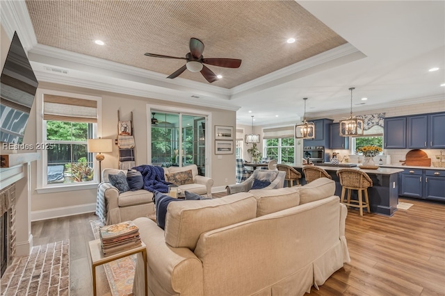 living room featuring ornamental molding, a brick fireplace, light wood-type flooring, and a tray ceiling