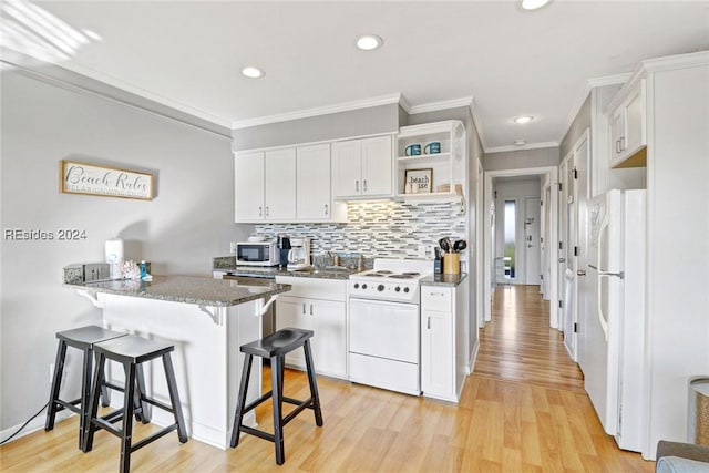 kitchen featuring white appliances, white cabinetry, dark stone countertops, light hardwood / wood-style floors, and kitchen peninsula