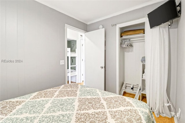 bedroom featuring ornamental molding, hardwood / wood-style floors, wood walls, and a closet