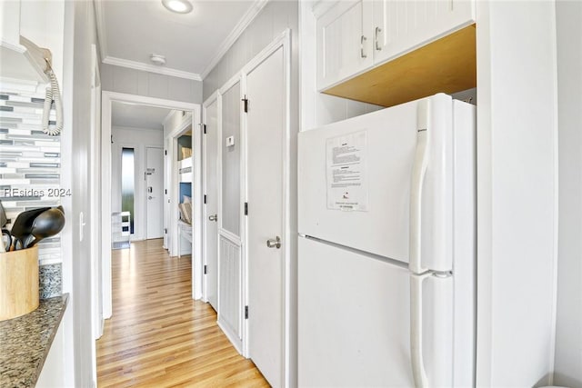 kitchen featuring crown molding, white refrigerator, dark stone counters, light hardwood / wood-style floors, and white cabinets