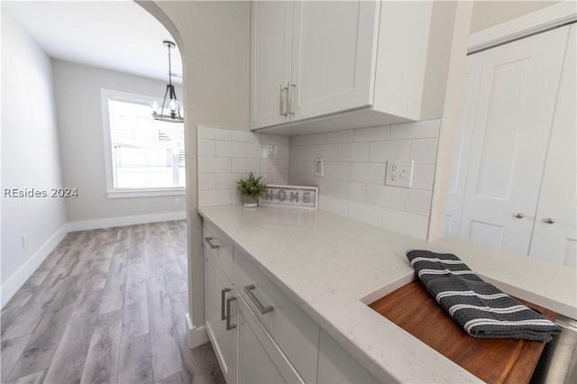 kitchen featuring pendant lighting, white cabinets, decorative backsplash, light stone counters, and light hardwood / wood-style flooring