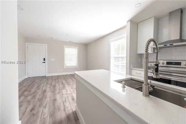 kitchen featuring tasteful backsplash, wall chimney exhaust hood, light wood-type flooring, and plenty of natural light