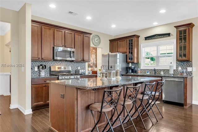 kitchen with a breakfast bar, sink, appliances with stainless steel finishes, a kitchen island, and dark stone counters