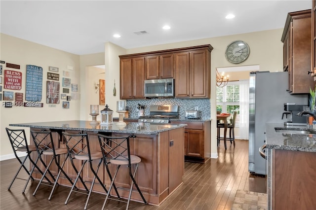 kitchen with sink, dark wood-type flooring, stainless steel appliances, decorative backsplash, and dark stone counters