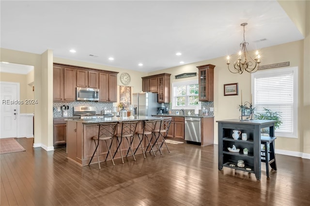 kitchen featuring pendant lighting, stone countertops, appliances with stainless steel finishes, a center island with sink, and decorative backsplash