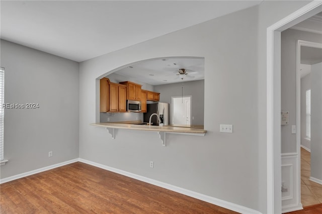 kitchen featuring light hardwood / wood-style flooring, a kitchen breakfast bar, kitchen peninsula, ceiling fan, and stainless steel appliances