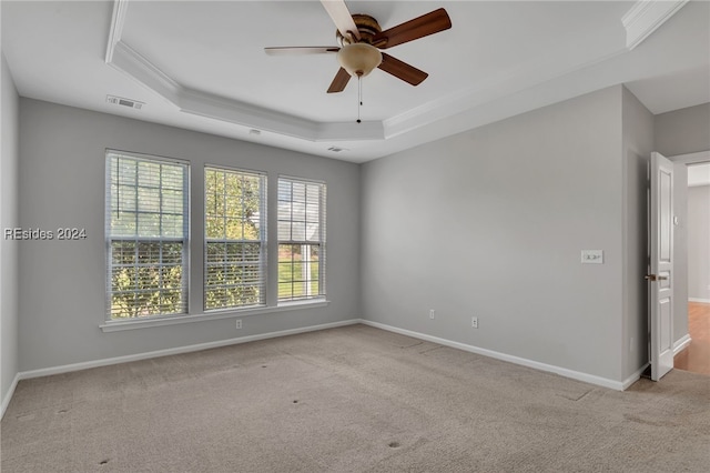 empty room with ceiling fan, light colored carpet, ornamental molding, and a tray ceiling