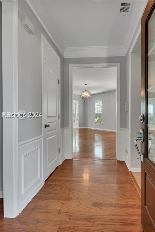 hallway with ornamental molding, a chandelier, and light hardwood / wood-style flooring