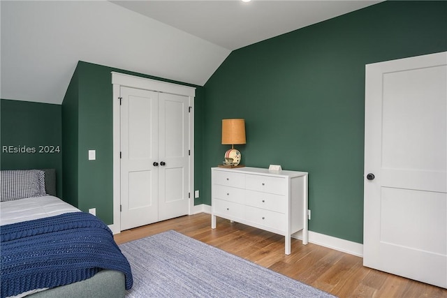 bedroom with vaulted ceiling, a closet, and light hardwood / wood-style flooring