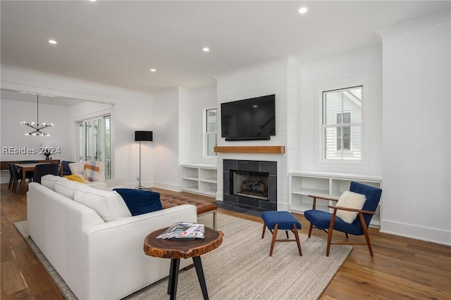 living room featuring a tiled fireplace, wood-type flooring, crown molding, and a chandelier