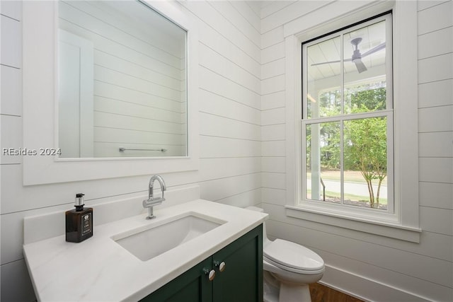 bathroom with vanity, a healthy amount of sunlight, wooden walls, and toilet