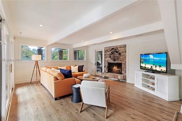 living room featuring beamed ceiling, light hardwood / wood-style floors, and a brick fireplace