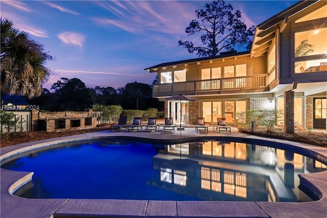 pool at dusk featuring a fireplace and a patio area