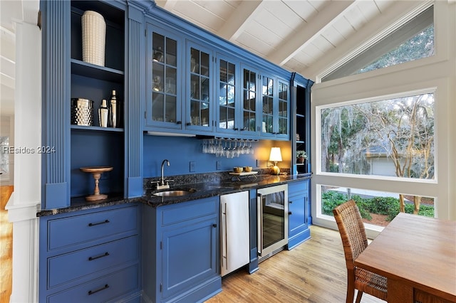 bar featuring blue cabinets, lofted ceiling with beams, sink, beverage cooler, and light hardwood / wood-style flooring