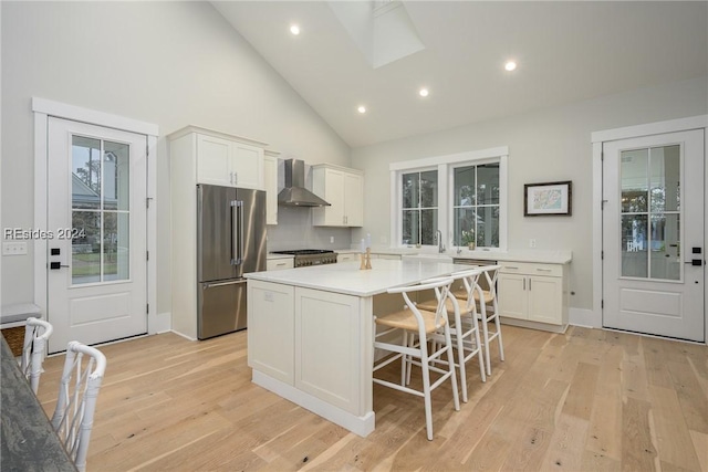 kitchen featuring wall chimney range hood, appliances with stainless steel finishes, white cabinetry, high vaulted ceiling, and a center island