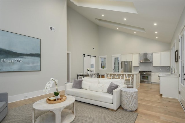 living room featuring a barn door, a towering ceiling, sink, and light hardwood / wood-style flooring