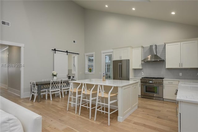 kitchen with a center island, high vaulted ceiling, high quality appliances, a barn door, and wall chimney range hood