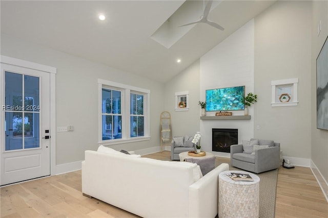 living room with ceiling fan, high vaulted ceiling, a large fireplace, and light wood-type flooring