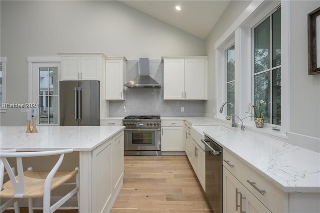 kitchen featuring white cabinetry, sink, backsplash, high end appliances, and wall chimney range hood