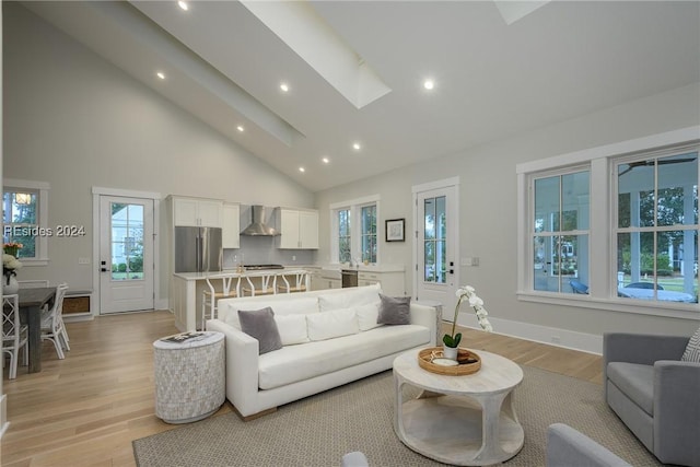 living room featuring a skylight, high vaulted ceiling, and light hardwood / wood-style floors