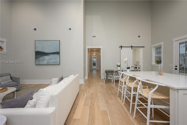 living room with light wood-type flooring, a barn door, and a high ceiling