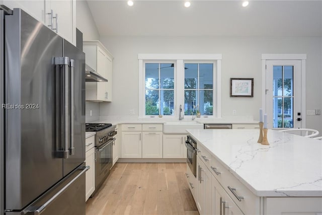 kitchen featuring premium appliances, light stone countertops, sink, and white cabinets