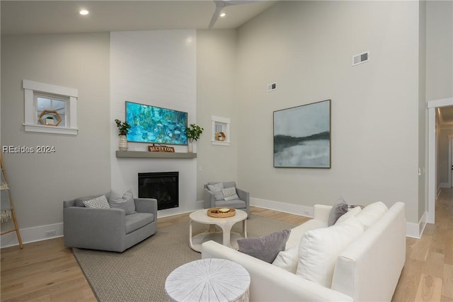 living room with a towering ceiling, a fireplace, and light hardwood / wood-style flooring