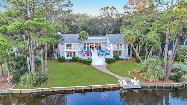 rear view of house featuring a balcony, a water view, and a lawn