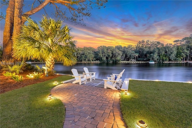 patio terrace at dusk featuring a lawn and a water view