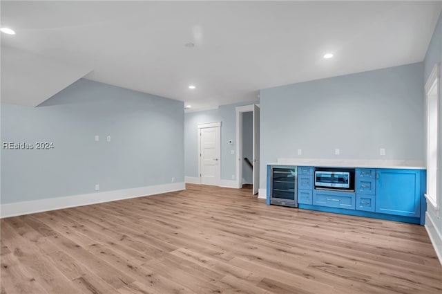 unfurnished living room featuring bar, beverage cooler, and light hardwood / wood-style flooring