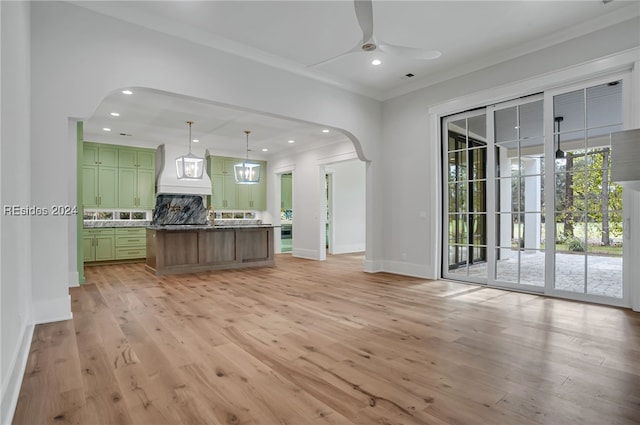 kitchen with crown molding, hanging light fixtures, backsplash, green cabinetry, and light wood-type flooring