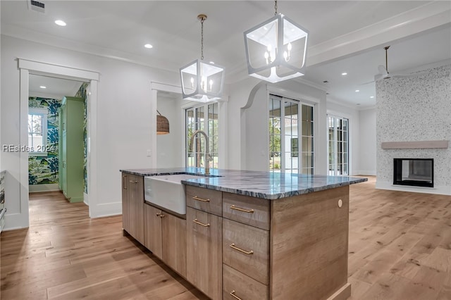 kitchen featuring stone countertops, hanging light fixtures, sink, and a center island with sink