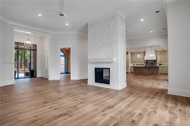 unfurnished living room featuring crown molding, light wood-type flooring, ceiling fan, and a fireplace