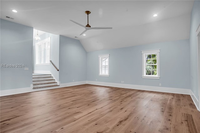 empty room featuring lofted ceiling, ceiling fan with notable chandelier, and light hardwood / wood-style flooring