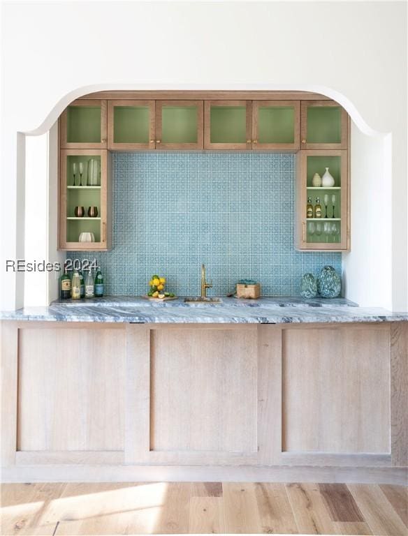 bar with light stone counters, backsplash, hardwood / wood-style floors, and sink