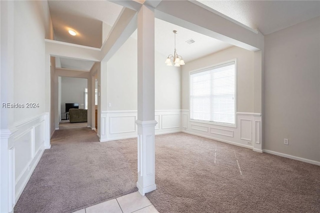 spare room with light carpet, a chandelier, and ornate columns