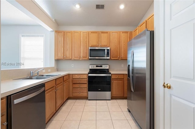 kitchen featuring stainless steel appliances, light brown cabinetry, sink, and light tile patterned floors